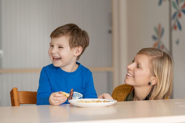 Kind sitzt am Tisch, isst Kekse und lacht mit der Therapeutin